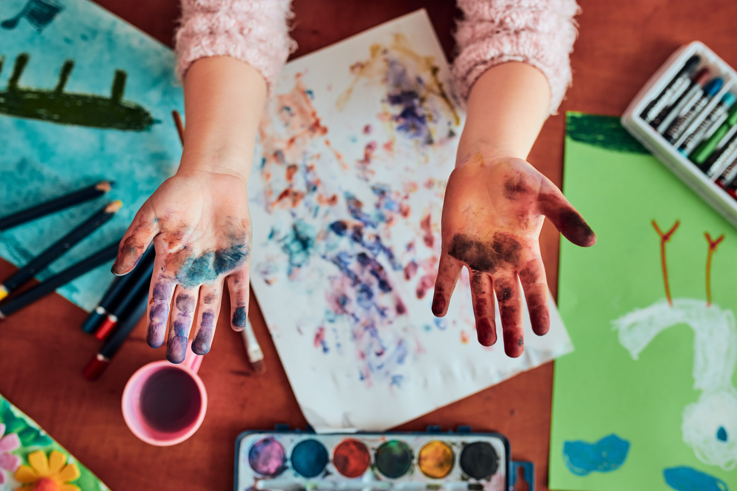 Little girl preschooler showing painted colourful hands Little girl preschooler showing painted colourful hands. Child having fun making a stamps on sheet of paper with painted hands during an art class in the classroom